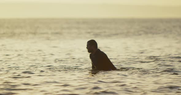 Side view of mid-adult caucasian male surfer sitting over surfboard in sea during sunset 4k alt
