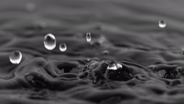 Super Slow Motion Shot of Water Drops Falling Into Water on Black Background at 1000 Fps. alt