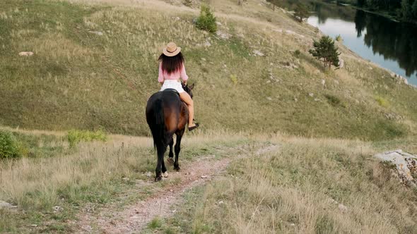 Beautiful Girl in Hat Riding a Horse Among the Hills. Female Rider Rides a Graceful Horse. Horseback alt