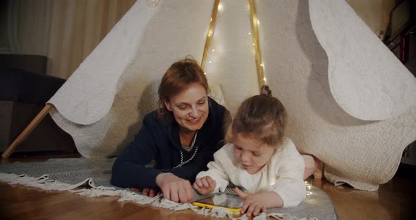 Happy Woman with Her Daughter at Smiling and Talking in Tent  Using Tablet alt