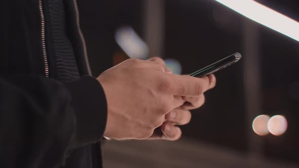 Detail shot with hands of a man writing-texting a message on the phone in the city at night alt