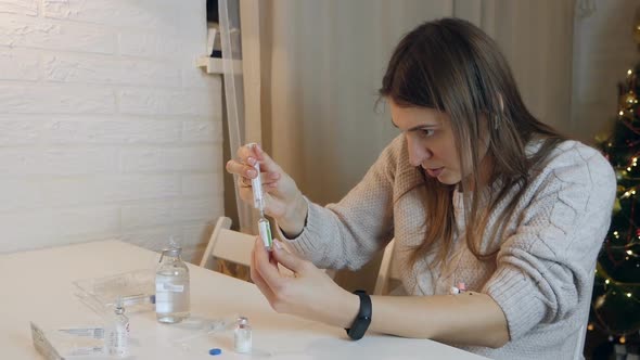 Young Woman Holding Ampoule with Medicines Inserting Needle Into Rubber Cap and Filling Syringe at
