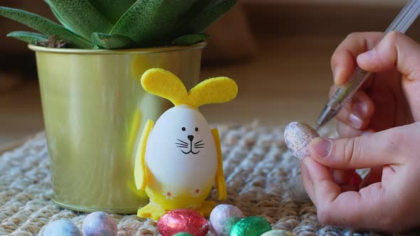 Girl draws a pattern on an Easter egg next to an egg in the shape of a rabbit