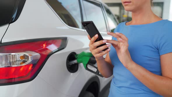 Woman Using Smartphone While Her Car Is Refueling alt