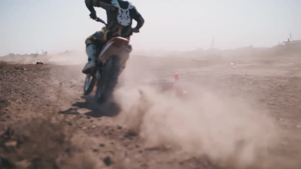 A biker rushes along a sandy track, leaving behind a cloud of dust.Slow motion.