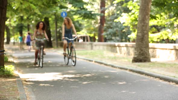 Couple of female friends riding bikes on the street at park on a sunny day alt