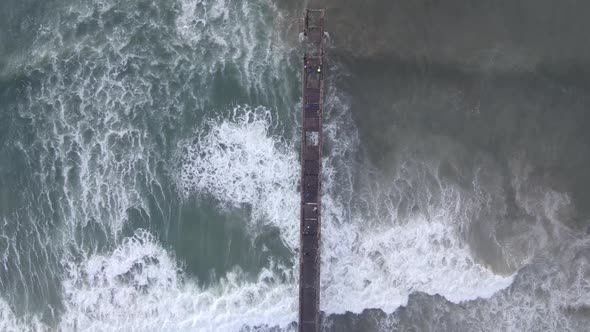 Drone Flying Over Pier with Waves Crashing in