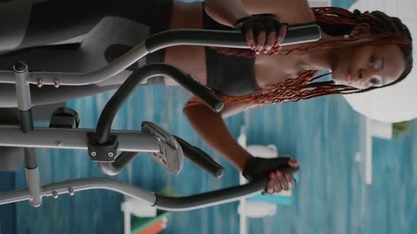 Verical Video Fit Athletic Black Woman Running on Elliptical Bike Watching Wellness Routine alt