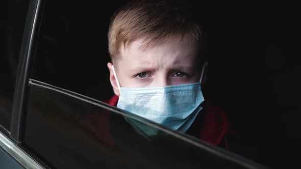 Kid in a Medical Mask Waving Goodbye and Looks Through the Car Window.