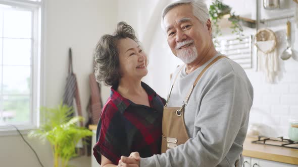 Asian mature senior couple is dancing and smiling in kitchen at home.