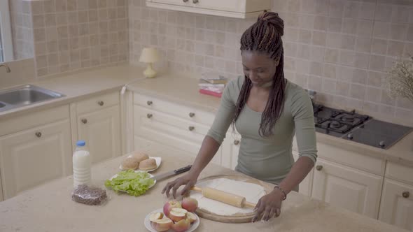 Beautiful Smiling African American Woman Rolling Dough with Rolling Pin for Apple Pie on the Modern alt