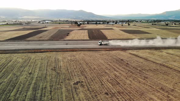 Aerial Footage Large White Truck with Truck Loaded with Rocks is Driving Down Gravel Road with Dust alt