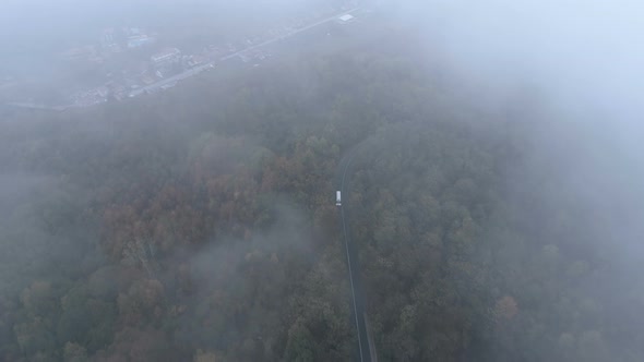Top View of White Truck Driving on Dangerous, Misty Forest Road. Drone Chasing White Bus on Foggy alt