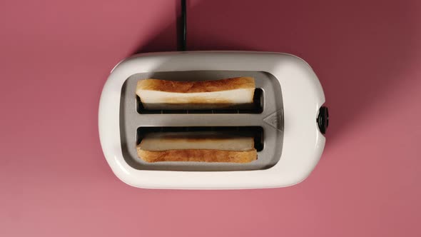 Roasted bread jump out from a white toaster on a pink table