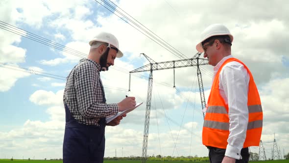 Two Engineers Working Near Transmission Lines. Manager Gives Task To Subordinate Near Transmission alt