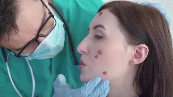 Doctor Examines a Young Woman with Large Moles on Her Face Close Up alt