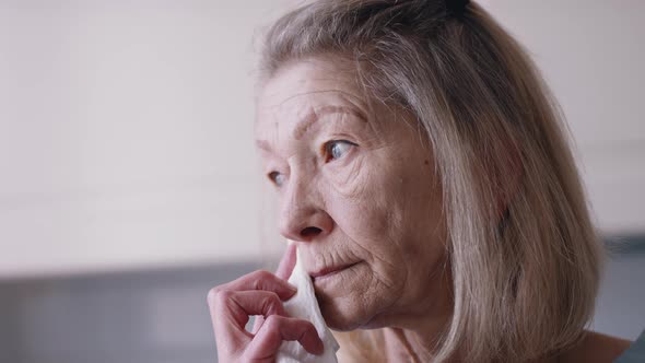 Pensive Old Woman Holding Napking Over Her Mouth alt
