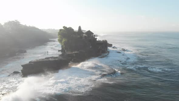 Aerial view over the water overlooking a Temple. The waves beat against the rocks and stones.