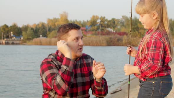 Father Showing Fish Bait To Daughter Near Lake