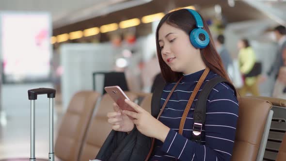 Young traveler woman use smartphone and listening music at airport