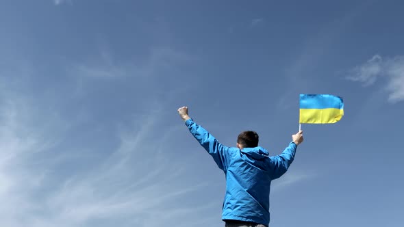 Man stands holding an Ukraine flag waving in slow motion at a bright overlook alt