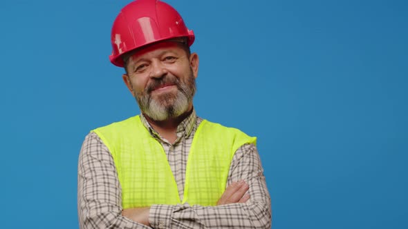 Smiling Senior Man Builder in Vest and Hardhat Against Blue Background