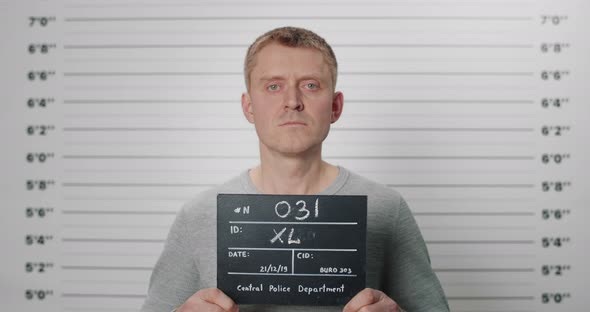 Portrait of Adult Man Holding Cardboard While Being Photographed in Police Department alt