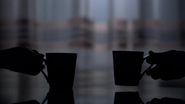 Dark silhouette of two ceramic cups, a man's and a woman's hand picks them up from the table alt