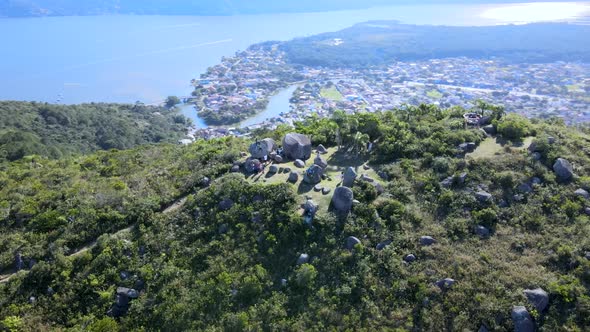 Aerial drone scene of mountain with rocks on top with city between ocean and river in background alt
