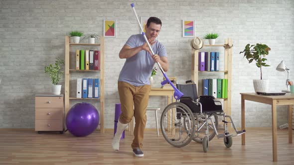 Cheerful Expressive Man with a Broken Bandaged Leg Plays Crutches Like a Guitar alt