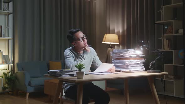 Asian Man Thinking And Looking At Paper Then Raising Index Finger While Working With Documents alt
