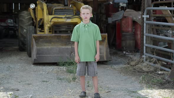 Slow motion push of boy with cleft lip standing in front of tractor. alt