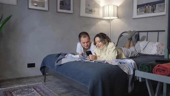 Young attractive Caucasian just married man and woman sitting in their bed late at night alt