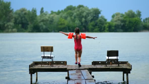 Little girl runs and jumps into the water from a wooden pier on a summer day