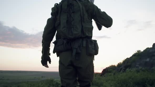 Confident Soldier Walks Forward and Holds a Sniper Rifle on His Shoulder Back View alt