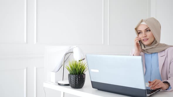 Attractive Relaxed Muslim Woman is Talking Mobile Phone Sitting on Her Workplace alt