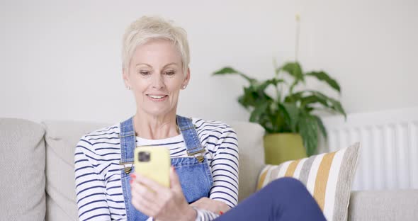 Mature woman sitting on sofa making video call on smartphone