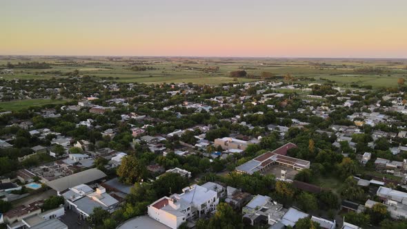 Dolly out flying over Santa Elisa countryside town houses surrounded by trees and farmlands in backg alt