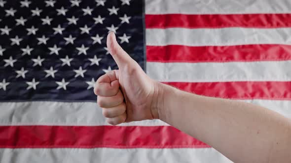 Thumbs Up Gesture Made with Caucasian Hand in Front of Blurry US Flag