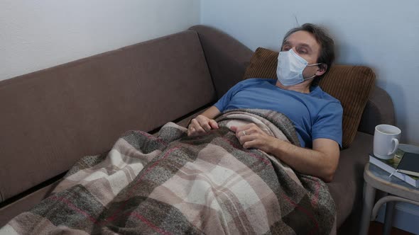 Sick Coughing Adult Man in Protective Mask Lying on a Bad at Home During Flu Pandemic