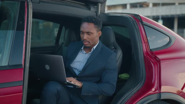 Man with Laptop Sitting Inside Charging Electric Car alt