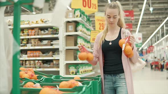 Young Blonde Woman is Taking Packages with Oranges in a Supermarket alt