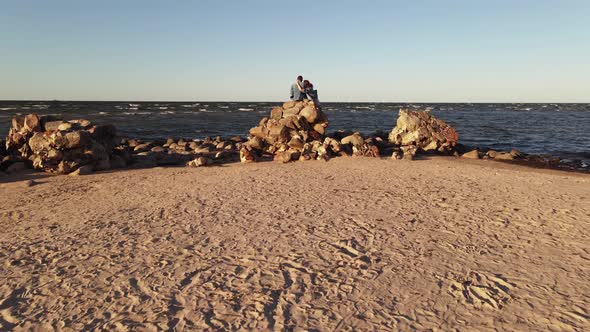 Fast Aerial Flight Just Above Couple Enjyoing Sunset on Rocky Beach at Cape Kolka alt