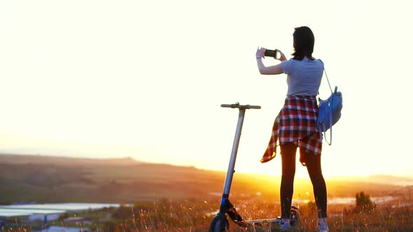 Girl Stands Next To the Electric Scooter Taking Pictures of the Mountain Landscape and Sunsetslow Mo alt