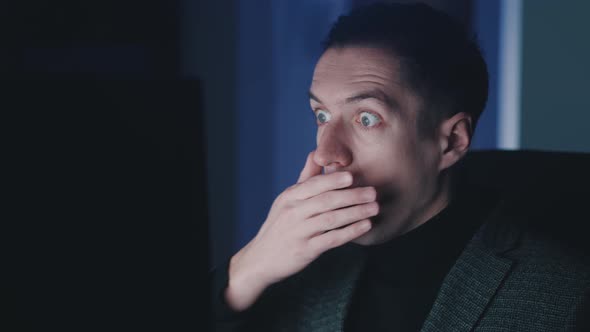 Afraid and Shocked Man Looking at Monitor Screen Takes Off Glasses and Cover His Mouth with His Hand