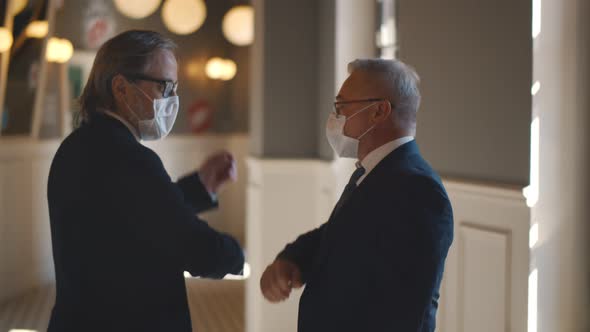 Mature Entrepreneurs in Medical Mask Greeting Touching Elbows alt