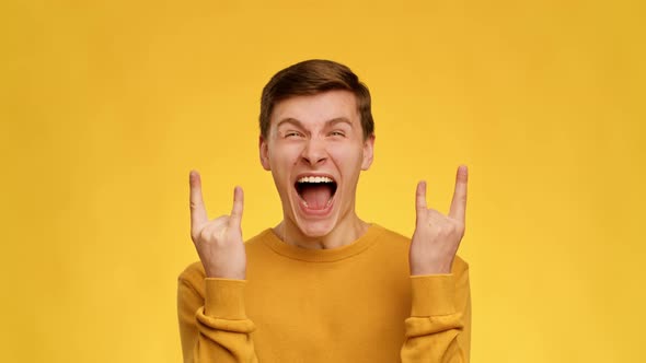 Emotional Guy Showing Rock Gesture Shouting On Yellow Background alt
