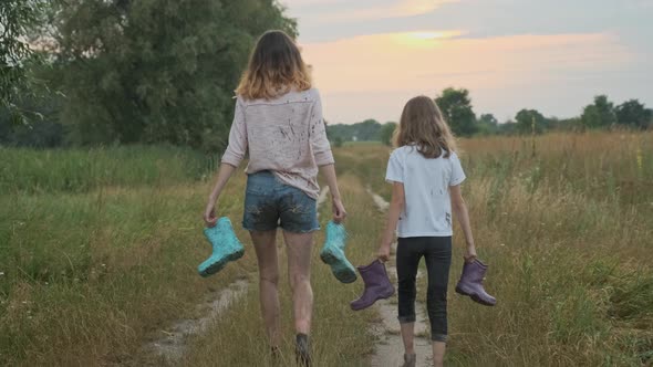 Two Happy Girls Sisters Walking After the Rain in Dirty Clothes Back View alt