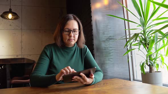 Middle Age Woman Sitting in Cafe with Tablet