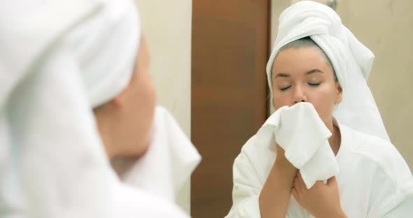 Woman Wipes Face Gently with Soft Towel Near Large Mirror